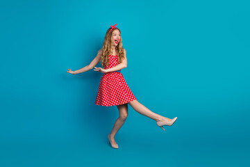 Smiling young woman in red polka dot dress posing playfully against blue background