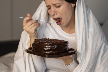 Depressed sad lonely woman eating cake in bedroom. Close-up. concept: junk food, cooking, baking and holidays. bad mood at the holiday. fucking valentines day. separation or dismissal from work
