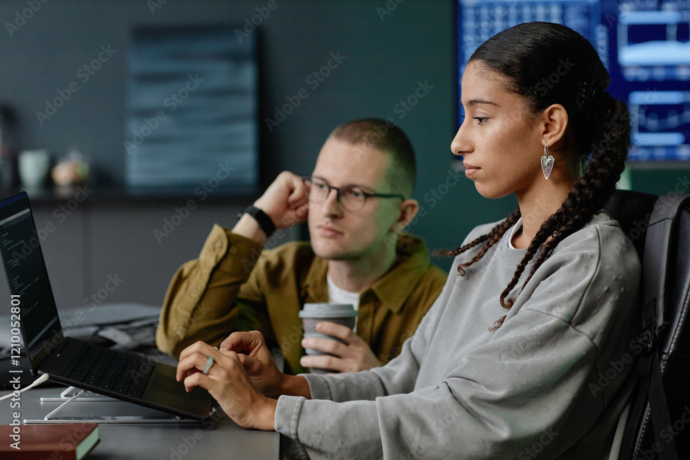 Poster side view of concentrated female it programmer coding on laptop collaborating with male colleague du