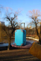 a blue travel suitcase stands on the hand of a man in a yellow jacket against the background of a lake