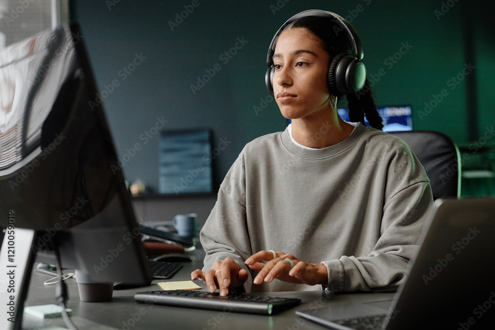 Poster medium shot of middle eastern female it engineer in headphones reading computer screen while coding 