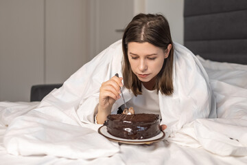 Sad depressed lonely woman young adult lying on bed eating cake. Eat unhealthy sugary foods. To experience the grief of loss. Mental Health. Depression. valentine's day or celebrating birthday alone