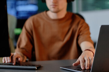 Cropped shot of unrecognizable male programmer using laptop and computer coding on multiple screens while working in IT company office, copy space