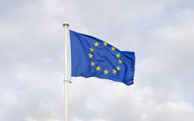 Flag of the European Union waving in the wind on flagpole against the blue sky. Close-up of single...