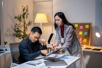 Asian businesswoman explaining using digital tablet to businessman working late