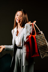 Woman carrying shopping bags expresses joy and excitement in a stylish outfit while enjoying a...