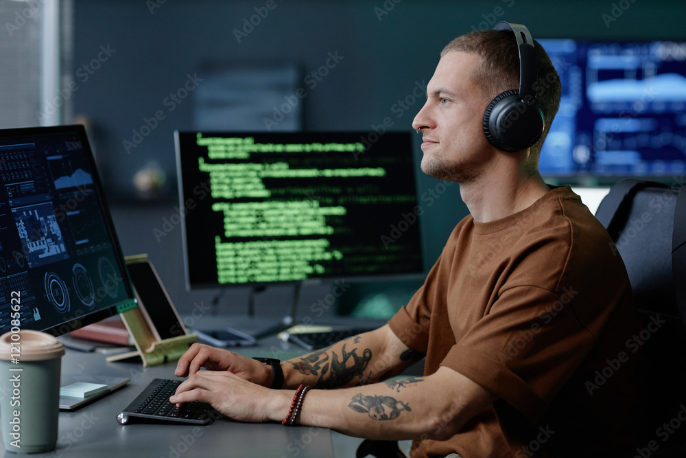 Aufkleber side view of handsome male programmer wearing headphones working at ease on desktop computer writing