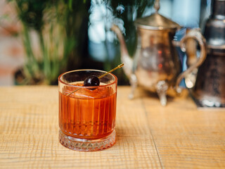 Boulevardier cocktail, bourbon-based drink with vermouth and Campari, garnished with a cherry, served in a crystal tumbler, wooden table, metallic teapot, natural light, close-up, warm bar ambiance