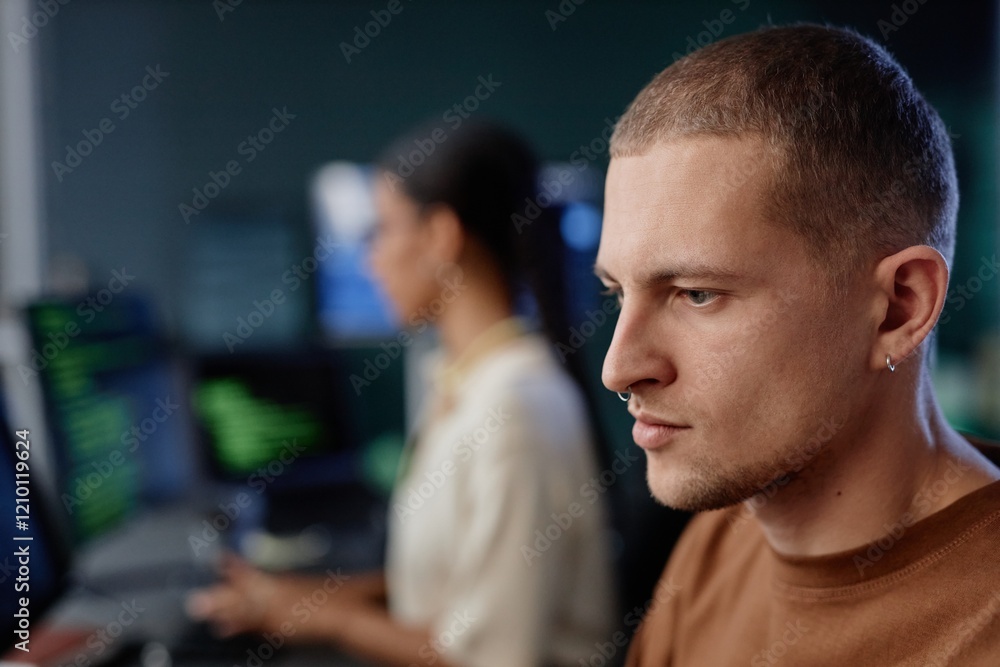 Poster side view portrait of concentrated male programmer with minimalist silver earring and septum immerse