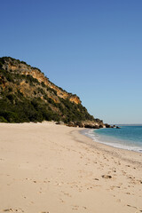 Fototapeta premium Beautiful beach with a blue ocean and mountains in the background. The beach is empty and the sky is clear Portinho da Arrábida beach, Setúbal, Portugal.