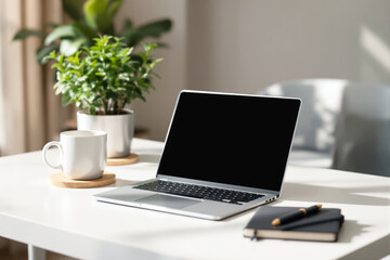 Fototapeta premium Minimalistic workspace with a laptop, mug, notebook, and plant on a white desk in a bright, cozy environment.