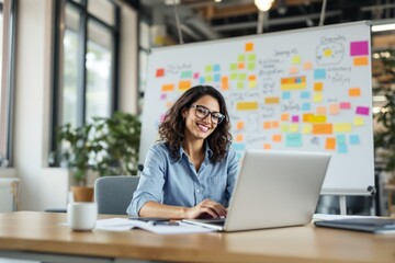 Smiling woman working on laptop in modern office, colorful sticky notes in background.