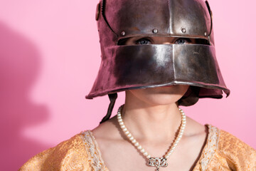 Woman in medieval steel helmet with pearl necklace and elegant attire against vibrant pink...