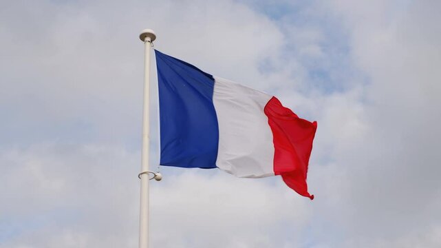 French national flag waving on cloudy sky background. The flag on a flagpole flutters in the wind. The image conveys the spirit of France: freedom, equality, fraternity.