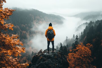 Obraz premium A lone traveler standing on a cliff overlooking a vast, fog-covered valley, with a small backpack and a distant gaze