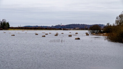 Flooded Field with Hay Bales Floating in Water on a Cloudy Day. Hay Bales in a Submerged Meadow During Seasonal Flooding.