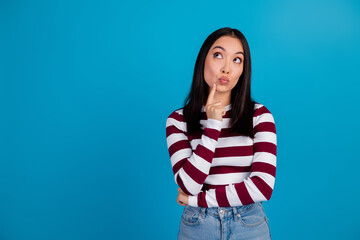 Young woman in a striped shirt thinking against a plain blue background