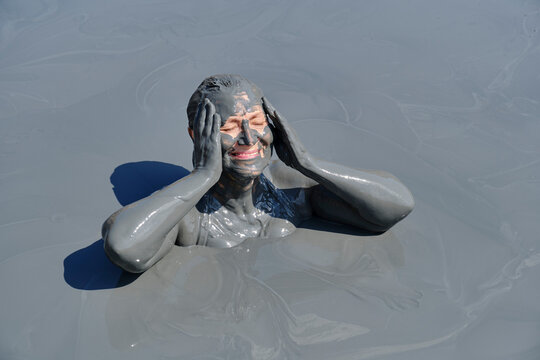 Senior woman enjoying mud bath with her face and body covered in therapeutic gray mud
