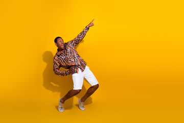 Young man posing in trendy shirt and white shorts against yellow background expressing excitement