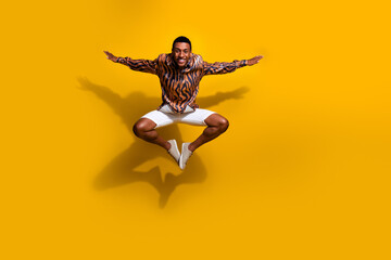Dynamic portrait of a young man joyfully leaping against a vivid yellow background, expressing...