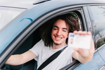Young man showing driving license while sitting in car
