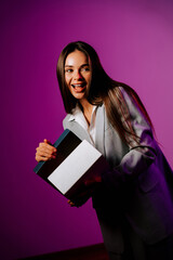 Woman in a grey suit holding a book with a playful expression against a purple background during a studio photoshoot