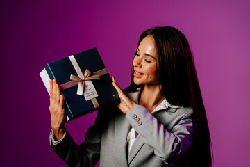 Excited woman in a suit holding a gift box with a purple background during a celebration