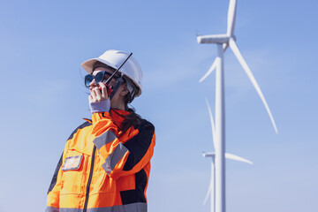 Fototapeta premium Engineer woman in hardhat with laptop and blueprint working on wind turbines at electricity power station background. Renewable energy, wind turbine generate electricity to produce energy .
