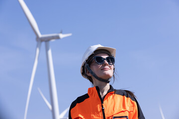 Engineer woman in hardhat with laptop and blueprint working on wind turbines at electricity power...