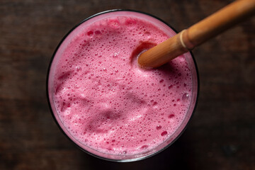 Raspberry banana smoothie with a bamboo straw on a wooden table, closeup, top view