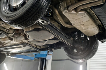 Modern car lifted on a hydraulic platform in an auto repair shop showing its undercarriage, exhaust...