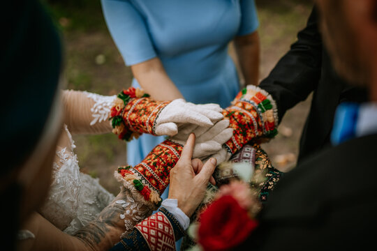  Close-up of hands in colorful traditional knitted mittens stacked together, symbolizing unity and tradition during a special ceremony.