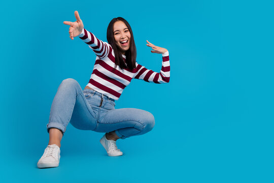 Young woman in striped shirt posing dynamically against bright blue background showcasing happiness and positive energy
