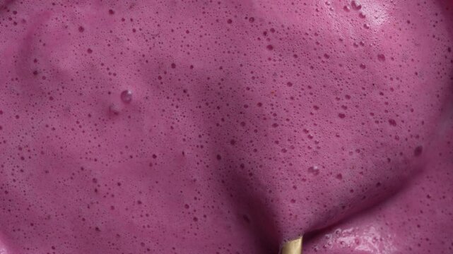 Glass of pink raspberry milkshake and spoon with foam, close up, top view. Fresh drink with the foam on the surface. Background of milk smoothie with bubbles