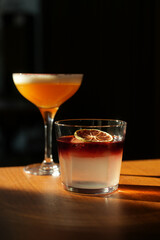 Two cocktail glasses with a slice of dry orange and ice cube on a wooden table.