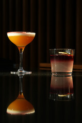 Two cocktail glasses with a slice of dry orange and ice cube on a wooden table.