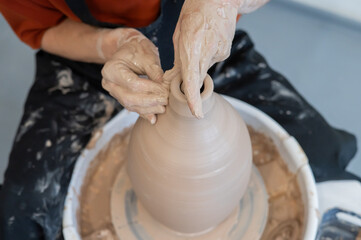 Close-up of a potter's hands making a ceramic vase on a potter's wheel. 