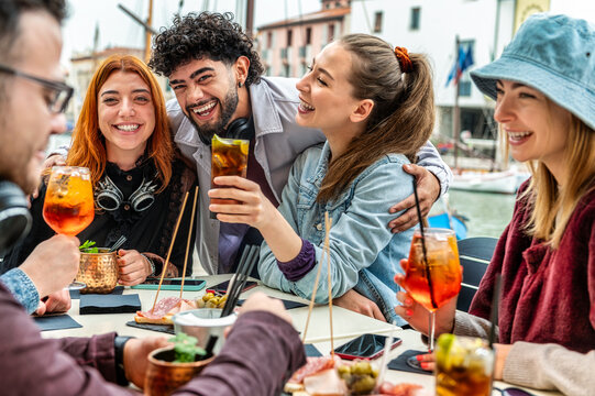Friends toasting spritz at cocktail bar restaurant - Young people having fun together toasting fancy drinks on happy hour time - Life style concept with guys and girls eating at dinner party