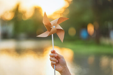 ESG and Clean Energy Concept. Close-up hand of woman holding wind turbine paper in park outdoor at sunset, Produce a green power and decrease carbon, World earth day, Sustainable resources.