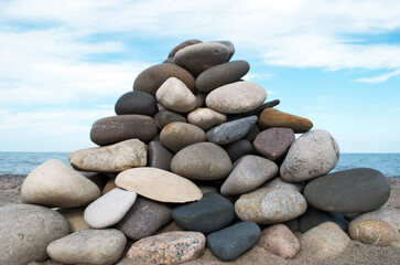 Triangular pile of stones stacked in foreground with blue sky white cloud background on beach