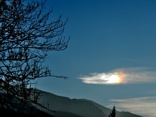 Colorful picturesque sky with Parhelion on Cirrostratus clouds over misty Tatras, Tatra Mountains in Poland and dark branches trees in autumn. Topics: optical phenomenon, air space, weather