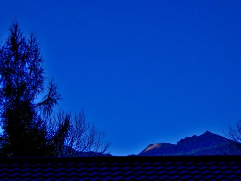 Abstract dark blue view with sky and dark horizon of mountain ranges with Kasprowy Wierch, Kasper Peak in Polish Western Tatras, Tatra Mountains over roof with roof tiles. Topics: Tatra National Park