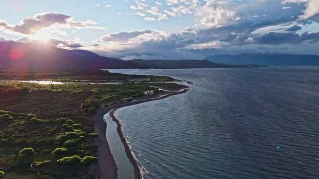 A heavenly delight in Argentina. Our drone footage captures the energy of the day as small waves crash against the shore, lined with green bushes. The towering Andes provide a dramatic backdrop.