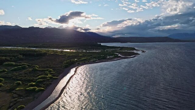 Nature's Breath: Los Antiguos. Our drone captures the serene lakeshore, fringed with vibrant green bushes, as a gentle breeze stirs the water, creating delicate ripples.