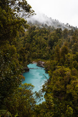 Turquoise calm water in Hokitika Gorge with fogs rolling through lush green forests on a rainy summer day (South Island, New Zealand)