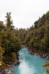 Turquoise calm water in Hokitika Gorge with fogs rolling through lush green forests on a rainy summer day (South Island, New Zealand)