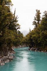 Turquoise calm water in Hokitika Gorge with fogs rolling through lush green forests on a rainy summer day (South Island, New Zealand)