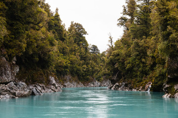 Turquoise calm water in Hokitika Gorge with fogs rolling through lush green forests on a rainy summer day (South Island, New Zealand)