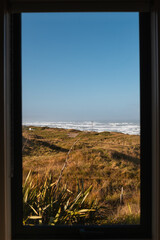 Window view onto shore of Cape Foulwind as seen from within with waves crashing on the beach (Cape Foulwind, South Island, New Zealand)
