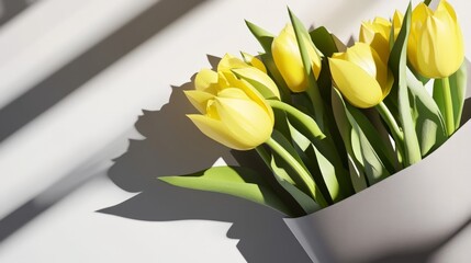 A bouquet of yellow tulips is sitting in a white vase. The flowers are in full bloom and are the center of attention. The vase is placed on a white background, which creates a sense of contrast